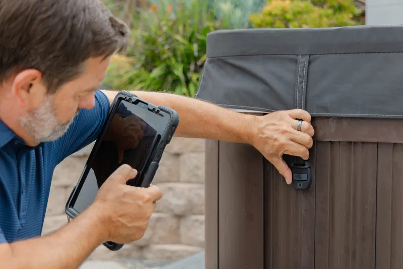 Inspector using a tablet to diagnose a covered hot tub cabinet.